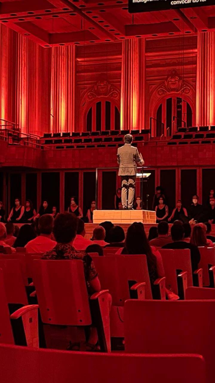 Teatro vermelho com instalação artística, público sentado e performer em palco